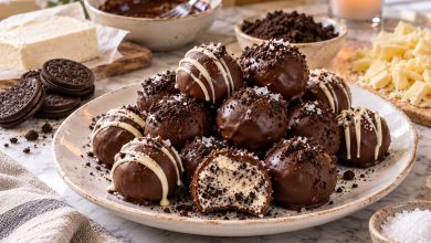 No-bake cookies and cream truffles dipped in chocolate with white chocolate drizzle on a white plate