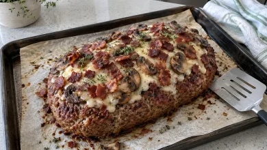 Bacon mushroom Swiss meatloaf topped with melted Swiss cheese, sauteed mushrooms and crispy bacon on a baking sheet