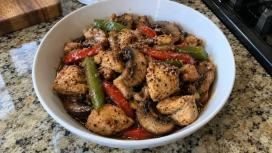 White bowl of black pepper chicken and mushrooms with seared chicken, browned mushrooms and bell pepper strips in glossy sauce