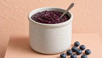 Crockpot blueberry butter in a speckled stoneware crock with a spoon and fresh blueberries