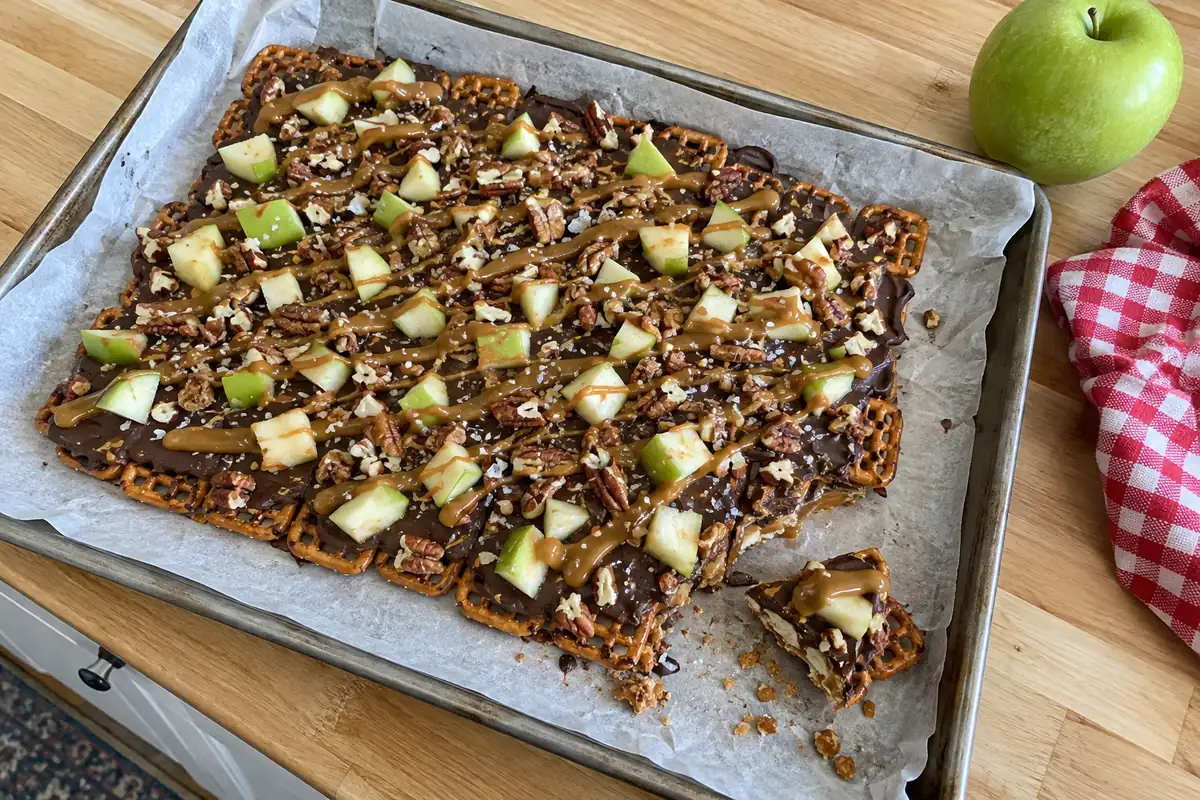 Caramel apple pretzel bark with chocolate, diced green apple, caramel drizzle and sea salt on parchment