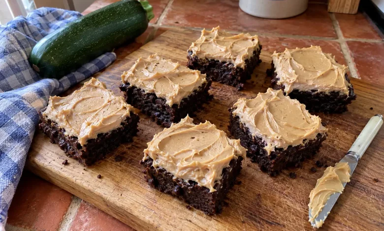 Chocolate peanut butter zucchini brownies with thick swirled peanut butter frosting on a walnut cutting board