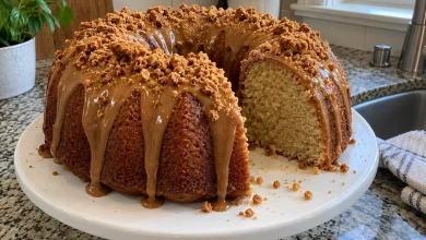 Cookie butter pound cake on a white cake stand with caramel-colored glaze dripping down, crushed spiced cookies on top and one slice cut out