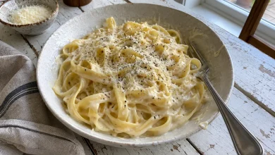 Bowl of fettuccine coated in thick cream cheese alfredo sauce topped with grated parmesan and black pepper