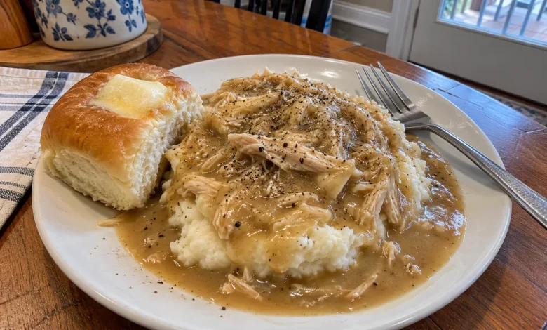 Plate of crockpot chicken and gravy over roasted garlic mashed potatoes with black pepper and a sweet dinner roll