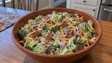 Terracotta-brown ceramic bowl of creamy crunchy broccoli salad with red onion, shredded cheddar, bacon bits and seeds on a home kitchen table
