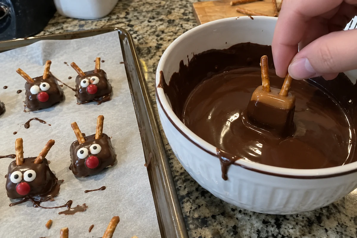 Dipping a caramel with pretzel antlers into a bowl of melted chocolate