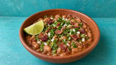 Drunken beans with crispy bacon, onion and cilantro in a terracotta clay bowl with a lime wedge
