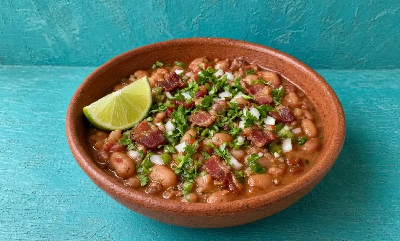 Drunken beans with crispy bacon, onion and cilantro in a terracotta clay bowl with a lime wedge