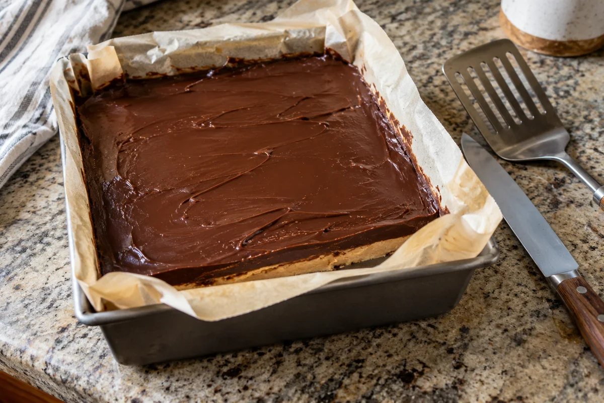 Pan of layered chocolate peanut butter fudge lined with parchment before cutting