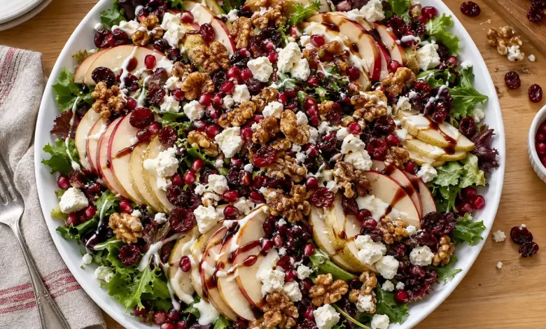 Harvest apple pear cranberry salad on a white platter with shingled fruit slices, greens, feta, candied walnuts, pomegranate arils and balsamic glaze