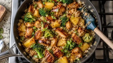 Top-down view of a Hawaiian chicken rice bowl in a large non-stick skillet with glazed chicken, jasmine rice, broccoli, pineapple chunks and sliced green onions