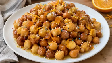 Mound of honey-glazed struffoli with colorful sprinkles and orange zest piled on a white plate