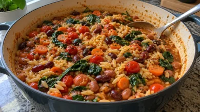 One-pot Mediterranean orzo and beans in a wide pan with a spoon on a home kitchen counter
