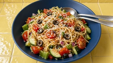 Million dollar spaghetti salad with cherry tomatoes, cucumber, peppers and black olives in a navy bowl