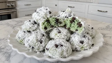 Mint chocolate chip snowball cookies coated in powdered sugar on a white plate, one broken open