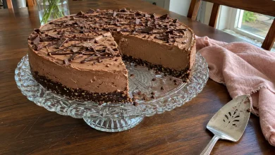 No-bake keto chocolate cheesecake with a chocolate drizzle and shavings on a vintage cake stand on a dark walnut table