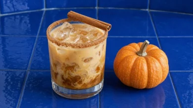 Pumpkin spice white russian over ice in a rocks glass with a cinnamon sugar rim and cinnamon stick next to a mini pumpkin
