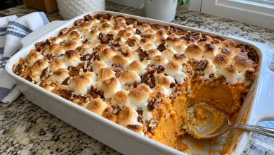 Baked sweet potato pumpkin casserole in a white baking dish with toasted mini marshmallows and pecans, one scoop taken out to show the orange filling