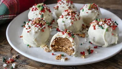 White-coated gingerbread truffles with colorful sprinkles on a white plate, one with a bite taken showing the tan gingersnap filling